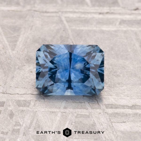 1.07-Carat Montana Sapphire (Heated) A 1.07-carat heated Montana sapphire with intricate facets rests on a textured gray surface, accompanied by the words "EARTH'S TREASURY" below it.