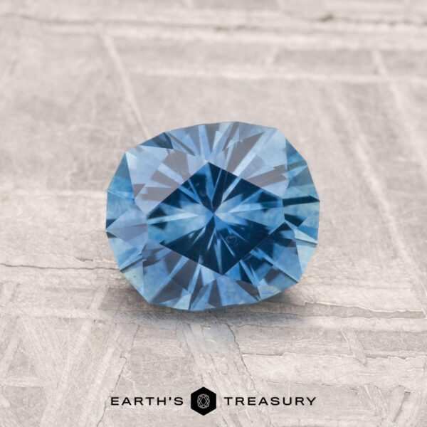 1.25-Carat Montana Sapphire (Heated) A 1.25-carat heated Montana sapphire is displayed on a textured gray surface, with the text "EARTH'S TREASURY" beneath it.