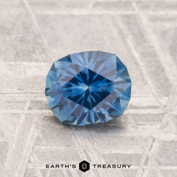 1.15-Carat Montana Sapphire (Heated) A 1.15-carat heated Montana sapphire with a cushion cut rests on a textured surface, with the text "EARTH'S TREASURY" below.