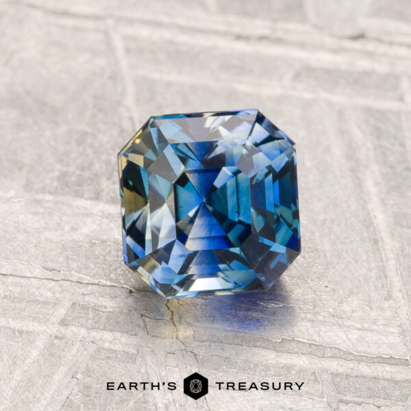 1.19-Carat Ceylon Sapphire (Heated) A 1.19-carat heated Ceylon sapphire with blue-green hues sits on a light, textured surface, featuring the "Earth's Treasury" text at the bottom.