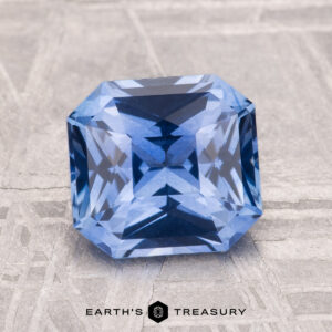 A 2.25-carat heated Ceylon sapphire with an emerald cut is displayed on a light patterned surface, with "Earth's Treasury" shown below.
