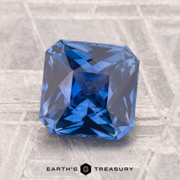 2.03-Carat Ceylon Sapphire (Heated) A 2.03-carat heated Ceylon sapphire, cut in a square shape, rests on a textured gray surface with "Earth's Treasury" displayed below.