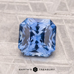 A 1.76-carat heated Ceylon sapphire in a rectangular step cut is shown on a textured gray surface, with "EARTH'S TREASURY" below.