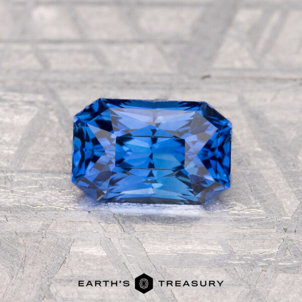 1.35-Carat Ceylon Sapphire (Heated) A rectangular, faceted blue 1.35-carat Ceylon sapphire (heated) rests on a textured metallic surface with "EARTH'S TREASURY" at the bottom.