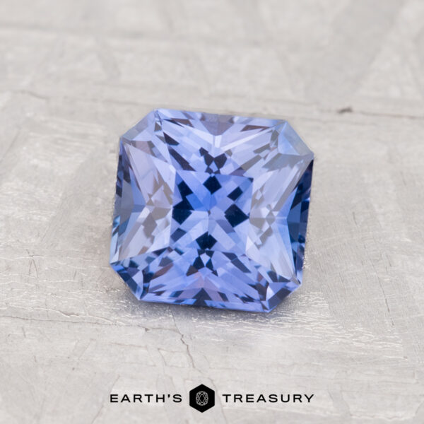 1.27-Carat Ceylon Sapphire (Heated) A 1.27-carat heated Ceylon sapphire with a square brilliant cut rests on a textured light gray surface. "EARTH'S TREASURY" is displayed at the bottom of the image.