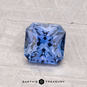 A 1.27-carat Ceylon Sapphire (heated), expertly square-cut with intricate faceting, sits on a textured surface with the words "EARTH'S TREASURY" below.