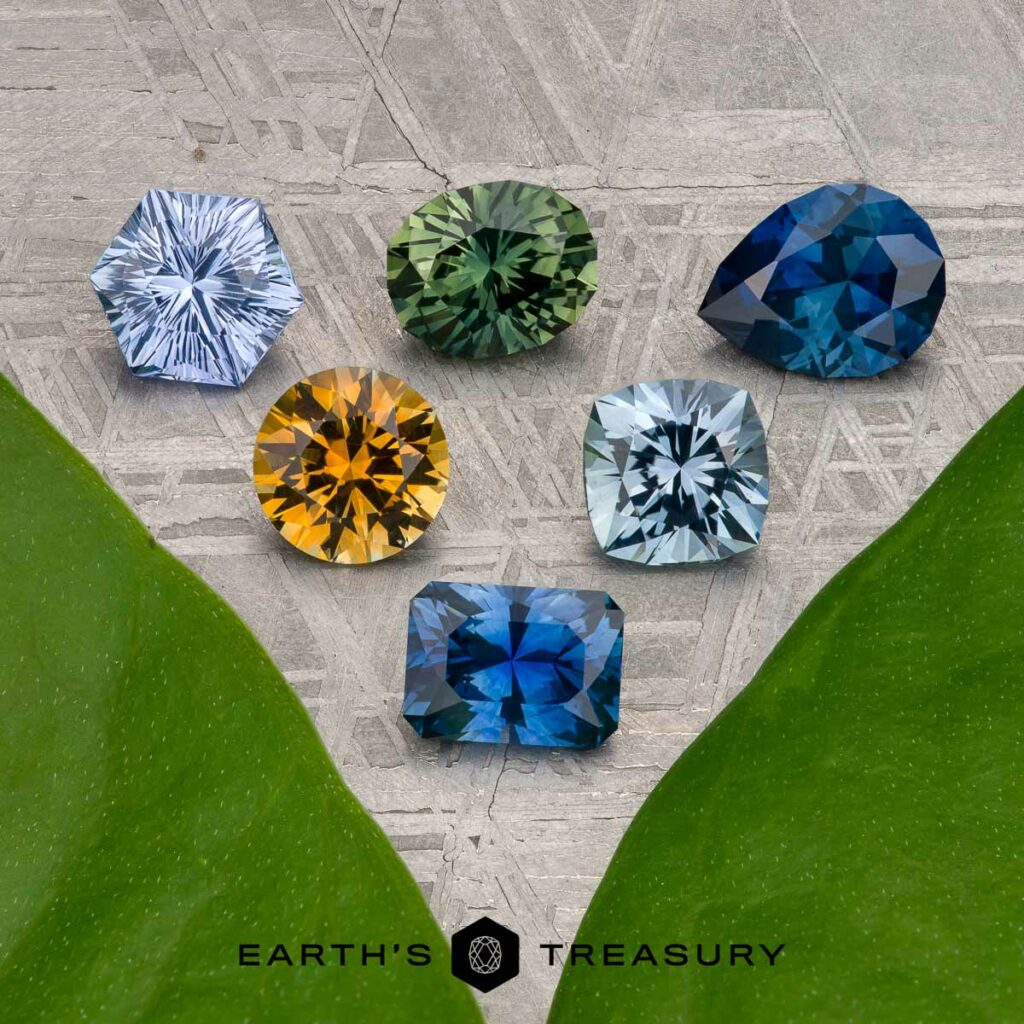 Six faceted gemstones in various colors and shapes are arranged on a patterned surface between two green leaves, with the Earth’s Treasury logo at the bottom. Product shown: "Stacked from 40 images. Method=B (R=10,S=7)".