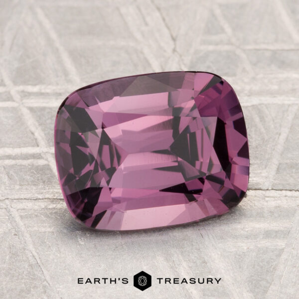 2.64-Carat Spinel A 2.64-carat cushion-cut purple spinel is displayed on a textured gray surface with the "Earth’s Treasury" logo beneath it.