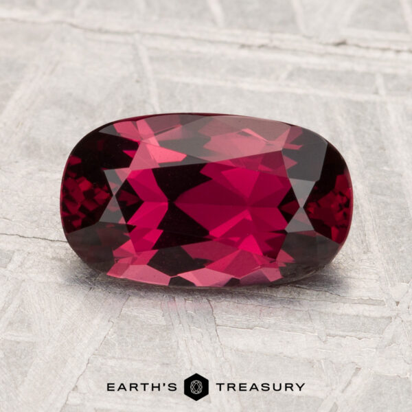 A 2.12-carat, deep red cushion-cut spinel is displayed on a light textured surface with the text "EARTH'S TREASURY" at the bottom.