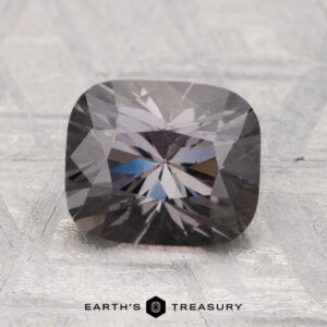 A 2.55-carat cushion-cut, dark gray spinel gemstone displayed on a light textured surface with the text "Earth's Treasury" at the bottom.