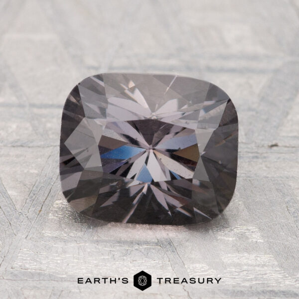 2.55-Carat Spinel A 2.55-carat cushion-cut, dark gray spinel gemstone displayed on a light textured surface with the text "Earth's Treasury" at the bottom.