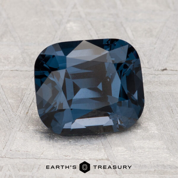 2.74-Carat Spinel A 2.74-carat, cushion-cut deep blue spinel is displayed on a light, textured surface with the text “EARTH'S TREASURY” at the bottom.