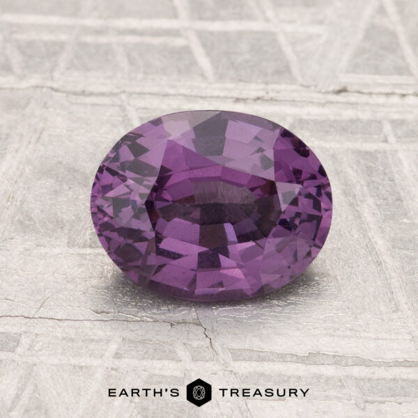 1.52-Carat Spinel A 1.52-carat oval-cut spinel gemstone is displayed on a textured light grey surface with "EARTH'S TREASURY" below.