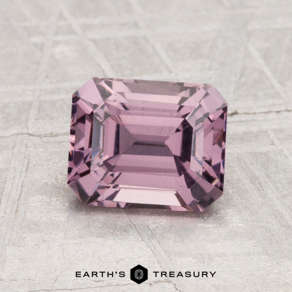 1.69-Carat Spinel A 1.69-carat, rectangular faceted light purple spinel is displayed on a textured gray surface with the text "EARTH'S TREASURY" below it.