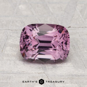 A 1.76-carat, cushion-cut purple spinel gemstone is displayed on a textured gray surface with "Earth's Treasury" at the bottom.