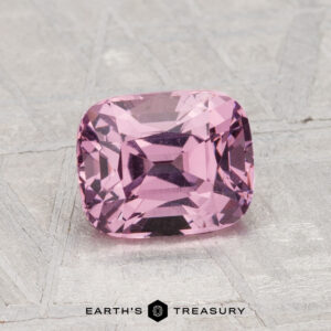 A 1.68-carat cushion-cut pink spinel is displayed on a textured gray surface with the text "Earth's Treasury" below.