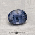 A faceted oval 1.29-carat Spinel gemstone resting on a light textured surface, with "EARTH'S TREASURY" text and logo below.