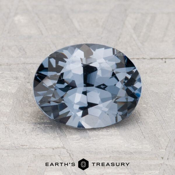 1.89-Carat Spinel A 1.89-carat round-cut blue-gray spinel shown on a textured light gray surface with the text "Earth's Treasury" below.