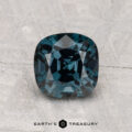 A 1.70-carat cushion-cut deep blue spinel is displayed on a textured gray surface, with the text "EARTH'S TREASURY" below.