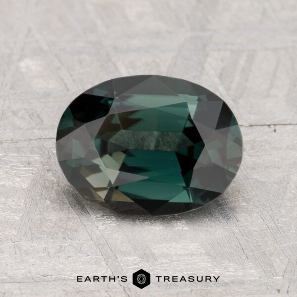 A 1.55-carat oval-cut green spinel rests on a textured light gray surface, with "EARTH'S TREASURY" displayed at the bottom.