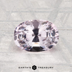 A 1.98-carat oval-cut pale pink spinel is displayed on a textured gray surface with "Earth's Treasury" at the bottom.