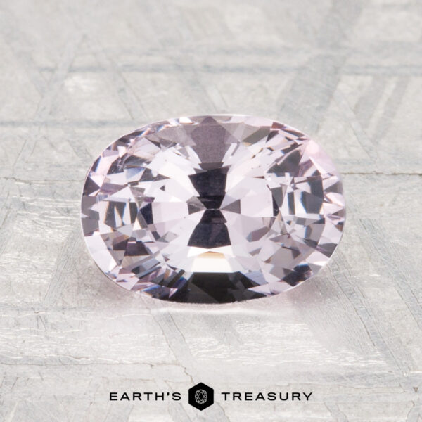 1.98-Carat Spinel A 1.98-carat oval-cut pale pink spinel is displayed on a textured gray surface with "Earth's Treasury" at the bottom.