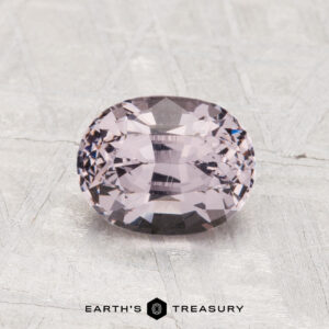 A 1.60-carat, cushion-cut lavender spinel rests on a textured gray surface, with the "Earth's Treasury" logo and text at the bottom.