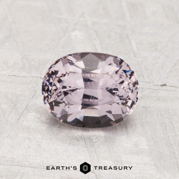 1.60-Carat Spinel A 1.60-carat, cushion-cut lavender spinel rests on a textured gray surface, with the "Earth's Treasury" logo and text at the bottom.