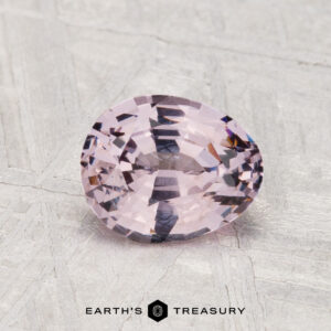 A 1.30-carat faceted oval light pink spinel is displayed on a textured gray surface, with "EARTH'S TREASURY" shown below.