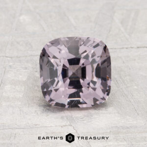 A 1.86-carat, cushion-cut light purple Spinel is displayed on a textured light gray surface with the "Earth’s Treasury" logo beneath.