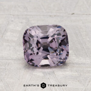 A 1.71-carat cushion-cut violet spinel is displayed on a textured light gray surface, with the text "EARTH'S TREASURY" at the bottom.