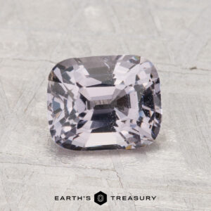 A 1.86-carat cushion-cut pale lavender spinel is displayed on a textured gray surface with "Earth’s Treasury" at the bottom.