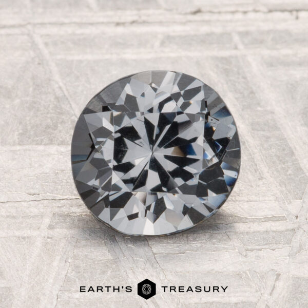 1.52-Carat Spinel A round brilliant-cut gray 1.52-carat spinel is displayed upright on a textured surface, with the text "EARTH'S TREASURY" below it.