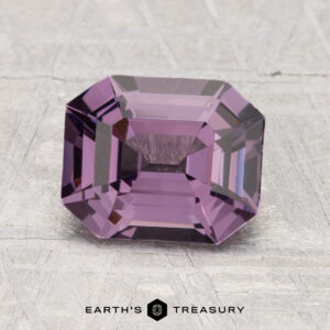 A rectangular, emerald-cut 2.12-carat Spinel gemstone in purple is shown on a light textured surface with "EARTH'S TREASURY" branding below.