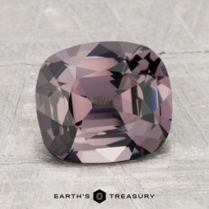 A 2.67-carat cushion-cut spinel gemstone in shades of purple and gray, displayed on a textured surface with "Earth's Treasury" written below.