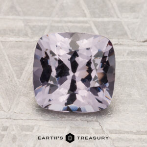 A 2.04-carat, cushion-cut spinel in light purple is displayed on a textured gray background with the text "EARTH'S TREASURY" below.