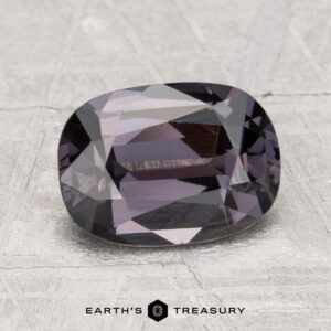 A 2.38-carat cushion-cut dark purple Spinel rests on a light textured surface, with "Earth's Treasury" shown at the bottom.