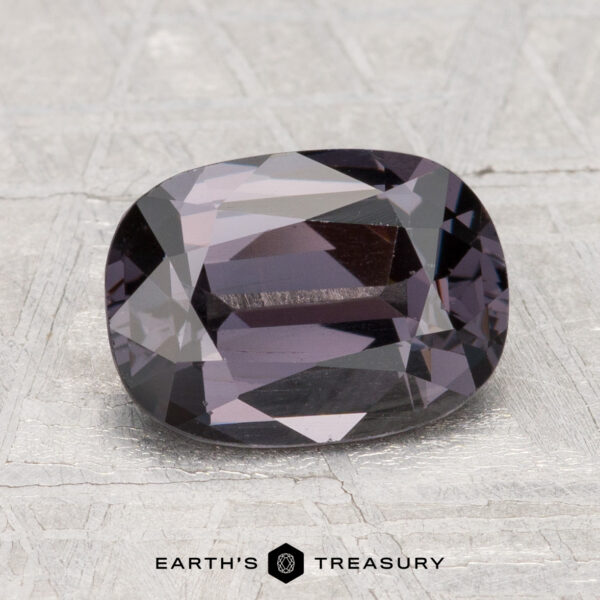 2.38-Carat Spinel A 2.38-carat cushion-cut dark purple Spinel rests on a light textured surface, with "Earth's Treasury" shown at the bottom.