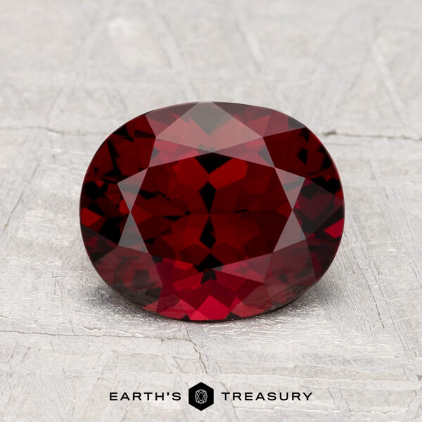 A faceted, oval-shaped 2.04-carat Spinel gemstone rests on a textured light gray surface with the text "EARTH'S TREASURY" below.