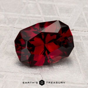 A 2.33-carat deep red spinel gemstone is displayed on a gray textured surface with the text "EARTH'S TREASURY" below it.