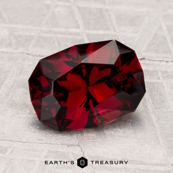 2.33-Carat Spinel A 2.33-carat deep red spinel gemstone is displayed on a gray textured surface with the text "EARTH'S TREASURY" below it.