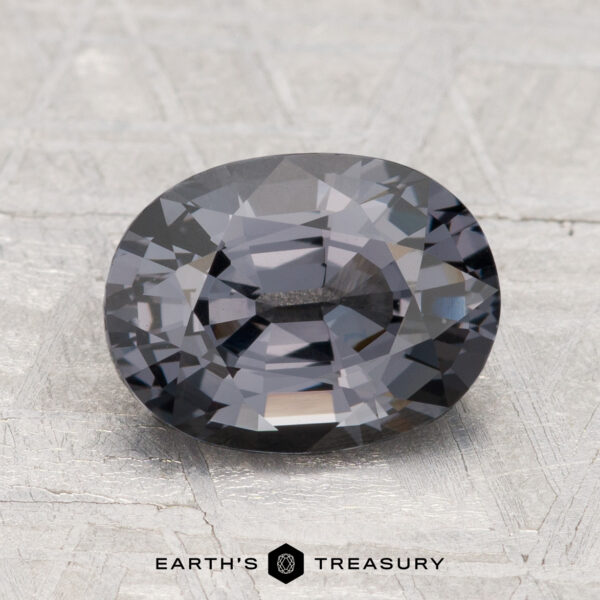 2.43-Carat Spinel A 2.43-carat, oval-cut dark gray Spinel displayed on a textured light surface with “EARTH'S TREASURY” below.