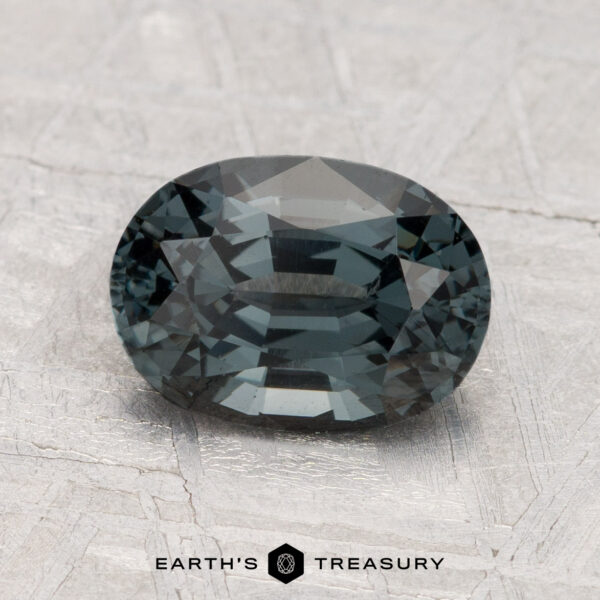 2.15-Carat Spinel A 2.15-carat spinel gemstone, oval-cut and dark blue-green, rests on a textured light gray surface with "Earth's Treasury" written below.