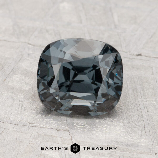 2.05-Carat Spinel A faceted, cushion-cut 2.05-carat Spinel in dark gray is displayed on a textured gray surface with “Earth’s Treasury” written below.