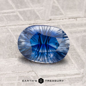 A faceted 1.51-carat Ceylon sapphire (heated) with a starburst pattern rests on textured silver, the "EARTH'S TREASURY" logo beneath it.