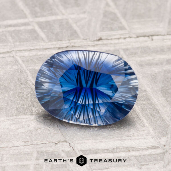 1.51-Carat Ceylon Sapphire (Heated) A faceted 1.51-carat Ceylon sapphire (heated) with a starburst pattern rests on textured silver, the "EARTH'S TREASURY" logo beneath it.
