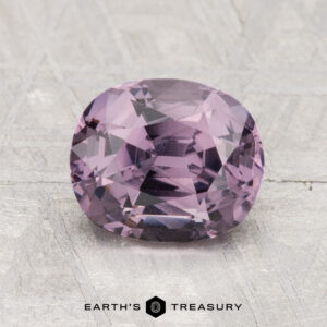 A 2.11-carat cushion-cut purple spinel is shown on a textured light gray surface with "EARTH'S TREASURY" at the bottom.