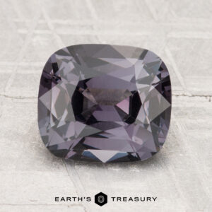 A 2.79-carat cushion-cut dark violet Spinel is displayed on a light textured surface with the text "Earth's Treasury" below it.