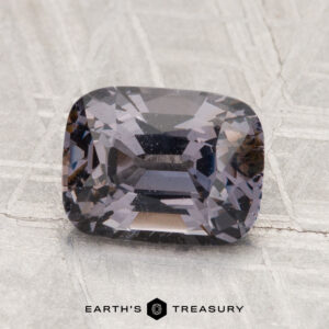 A 2.35-carat faceted spinel with a dark, smoky hue rests on a textured gray surface. "Earth's Treasury" appears at the bottom of the image.