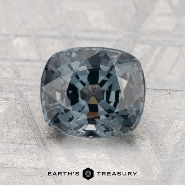 2.19-Carat Spinel A 2.19-carat, cushion-cut dark gray spinel rests on a textured surface with "EARTH'S TREASURY" displayed beneath.